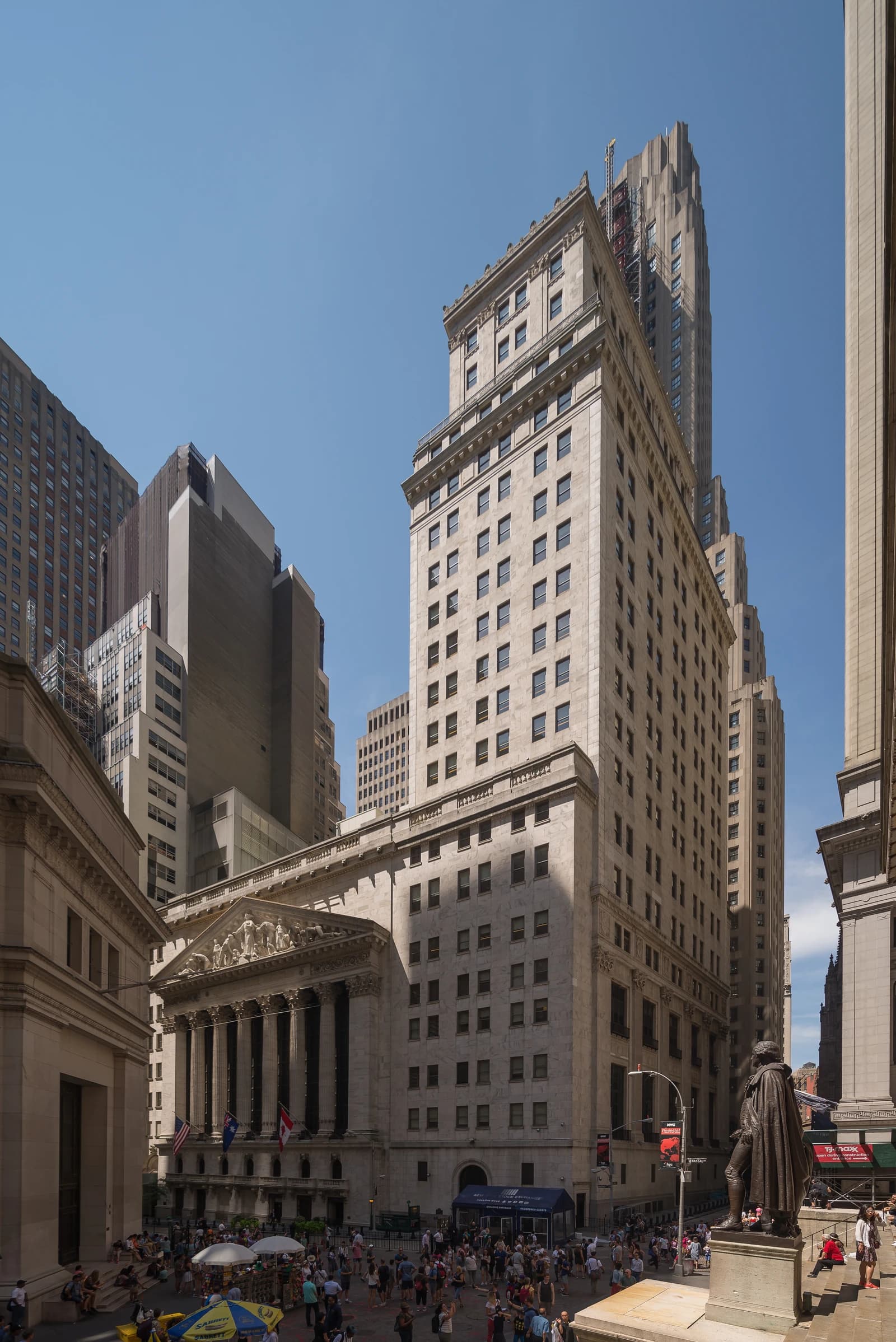 Exterior of the New York Stock Exchange building on Wall Street, people walk below.