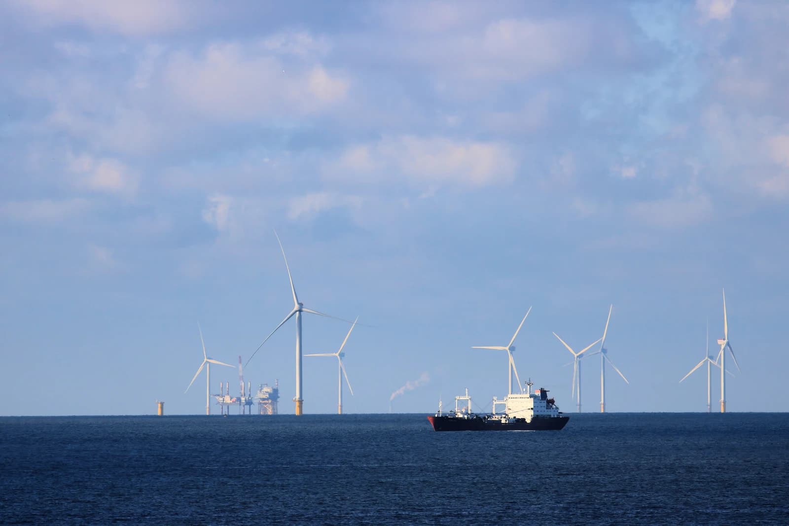 Oil tanker sailing on deep blue water with numerous wind turbines and oil rigs visible.