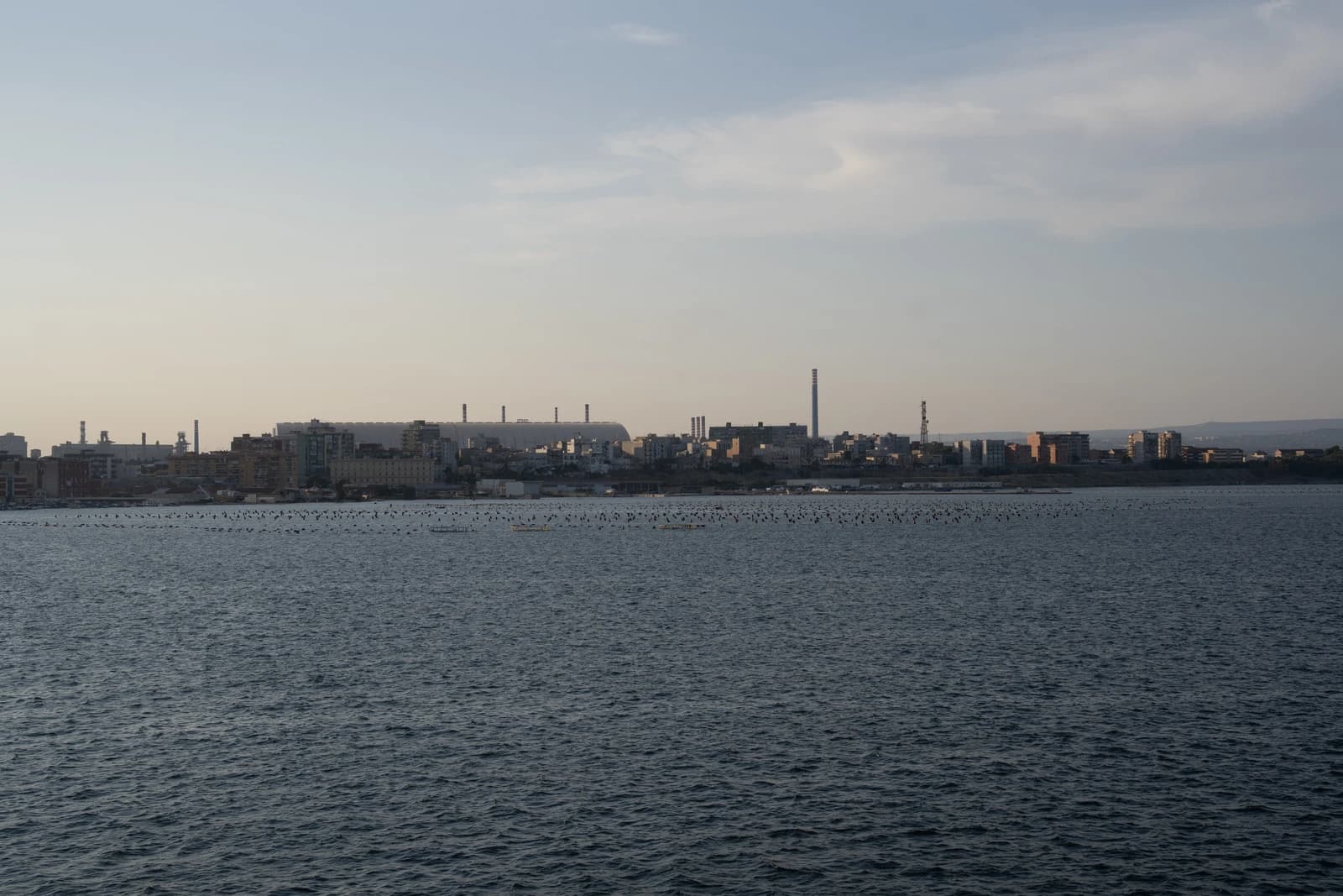 Taranto steelworks from across the water, showing industrial skyline and chimneys.