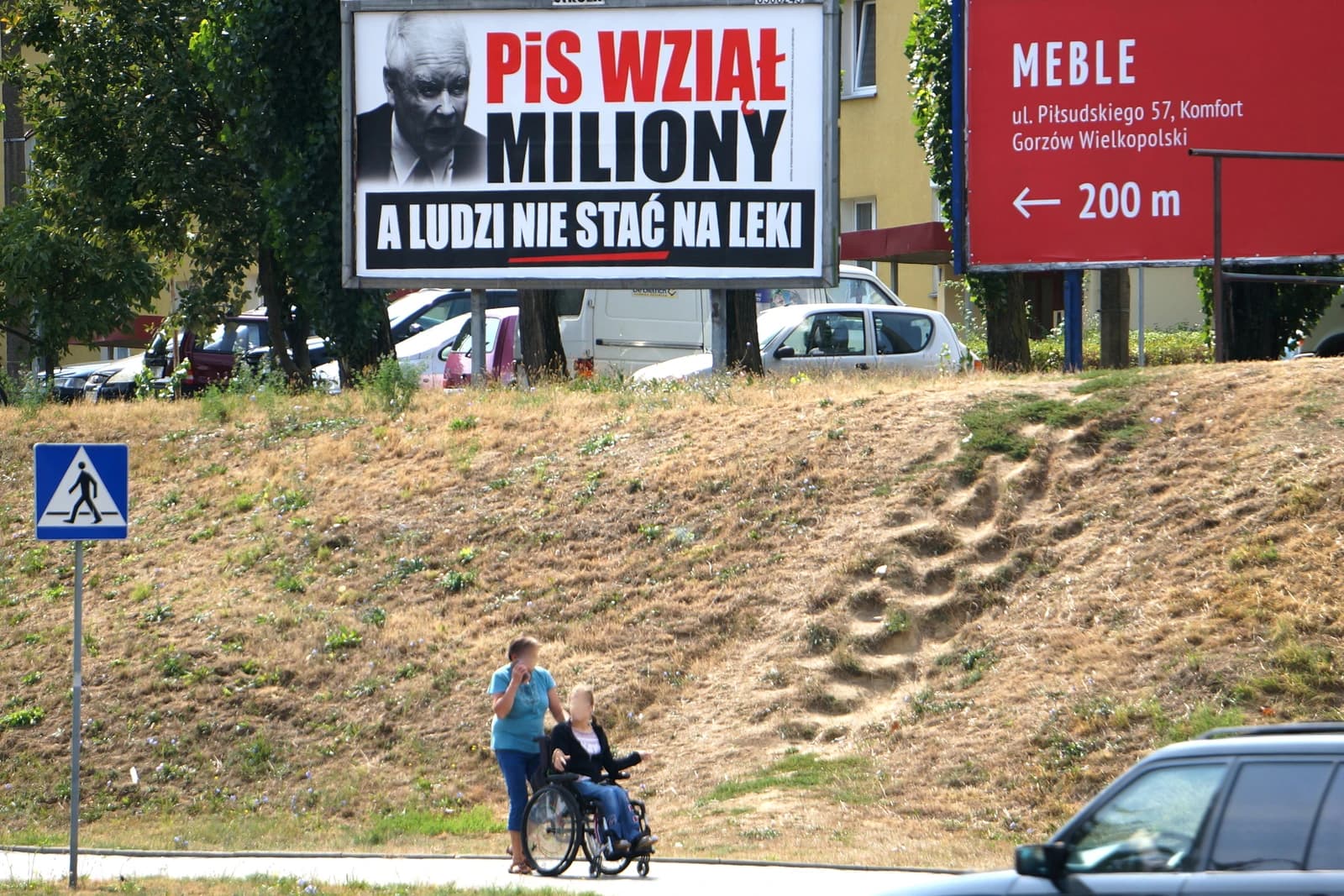 Billboard with a man's face and text 'PiS wziął miliony, a ludzi nie stać na leki'.