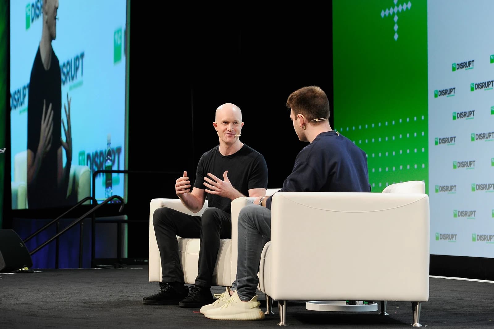 Man with bald head speaking on stage at TechCrunch Disrupt event to another man.