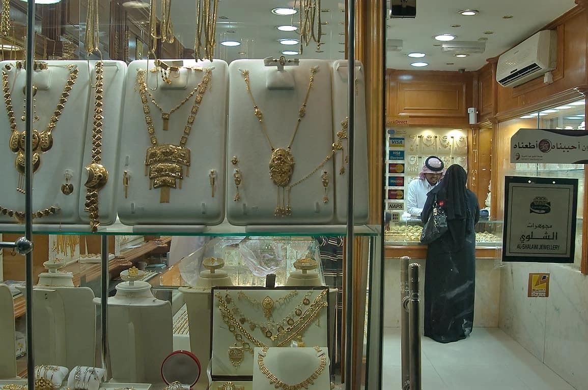 A woman in a black abaya is seen from behind, standing at a counter in a jewelry shop.