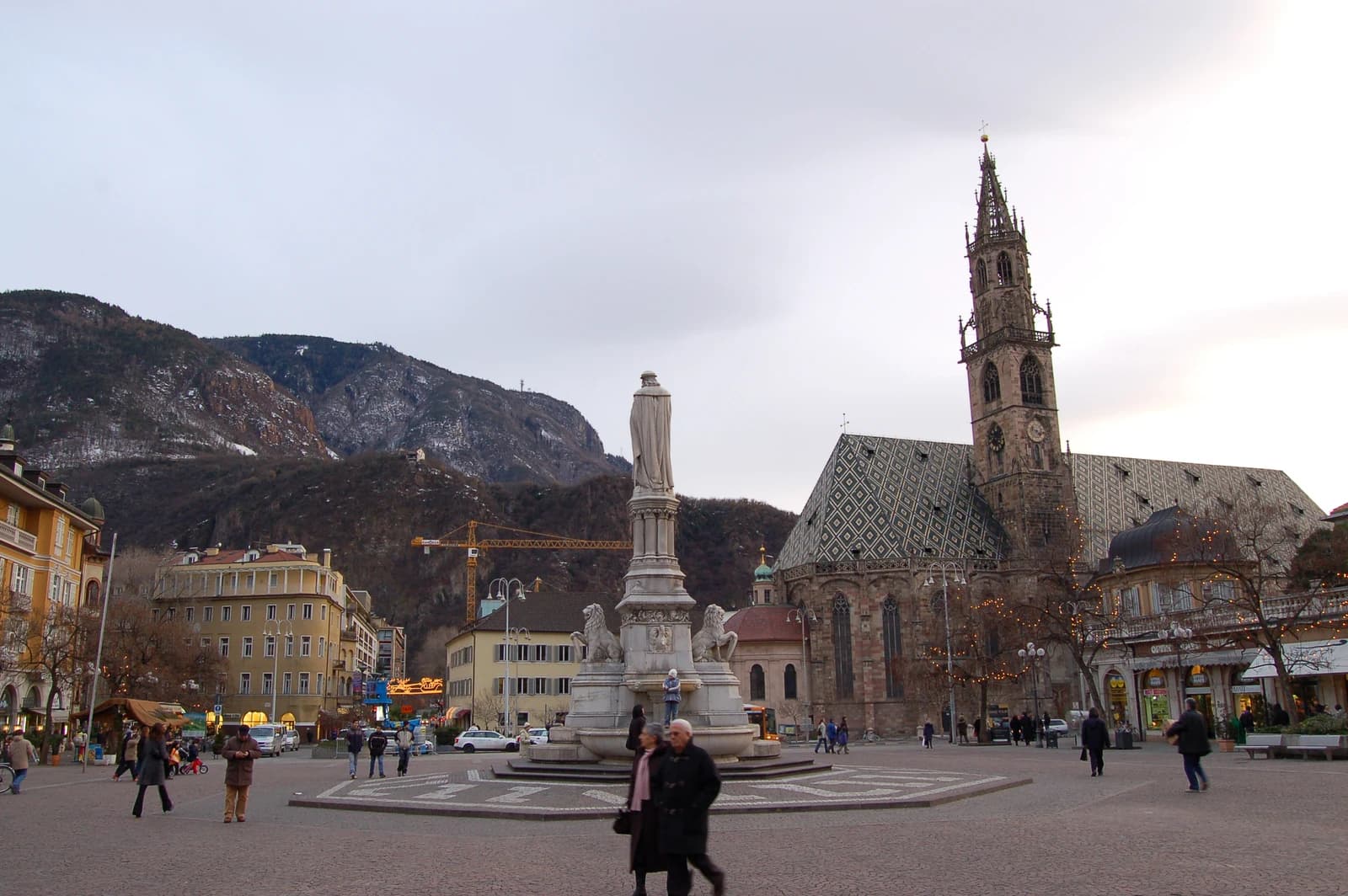 View of Bolzano's central square with a statue, people, and historic buildings including a church.