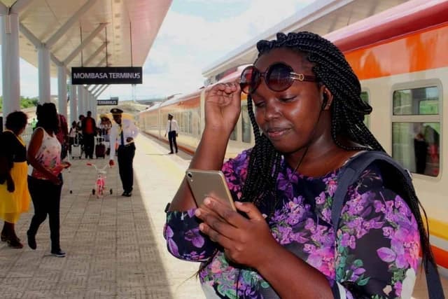 Passenger holding sunglasses and phone on a train platform in Mombasa.
