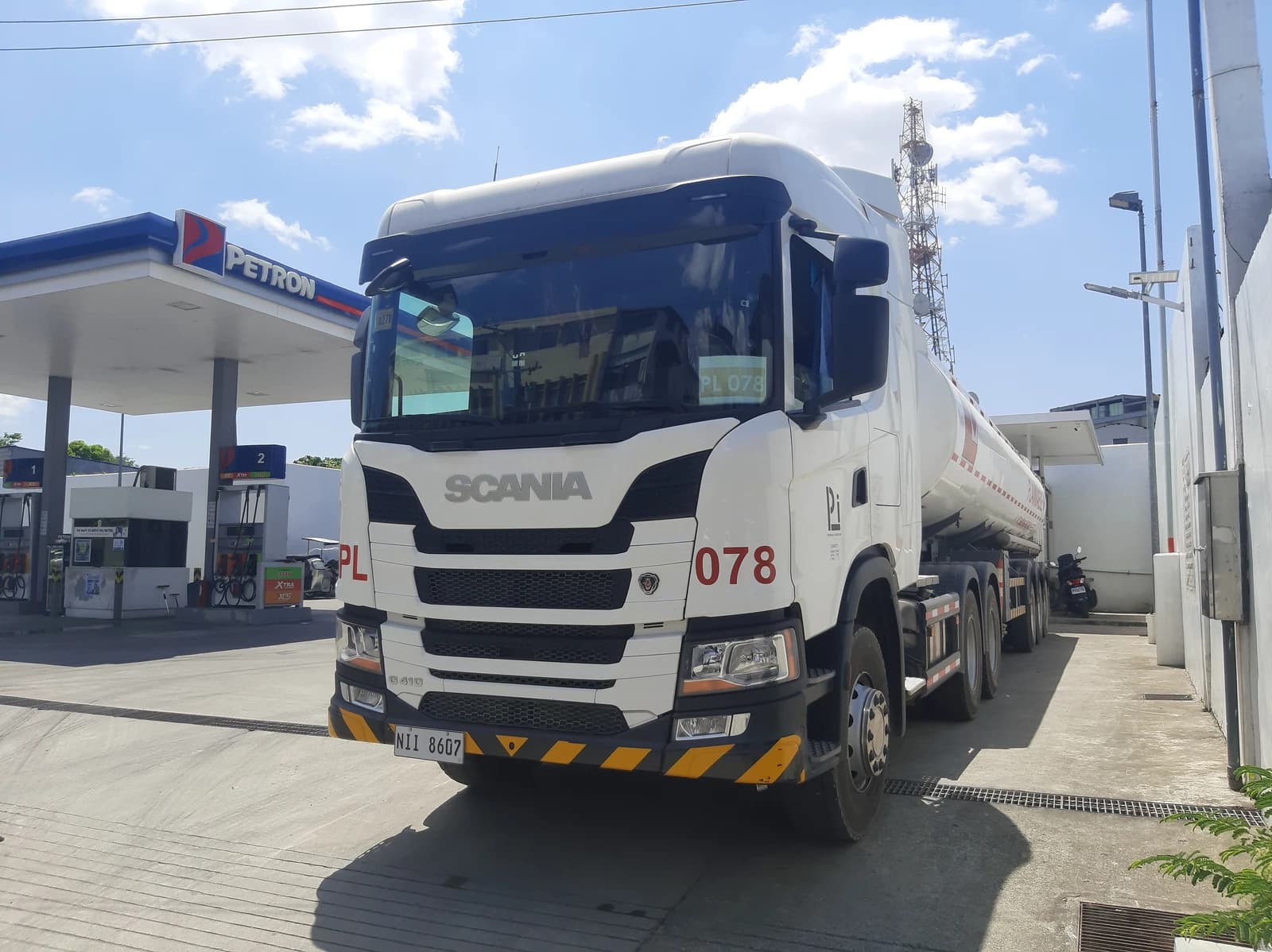 Scania G410 tractor truck with an attached fuel tanker trailer at a gas station.