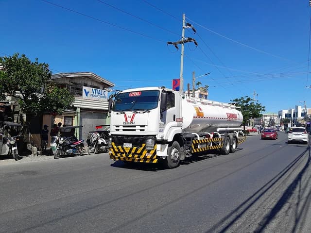 Isuzu FVM fuel tanker truck driving on a multi-lane street during the day.