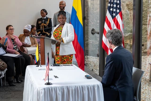 US Secretary of State Antony Blinken sitting with his back to the camera, facing a speaker at a podium.