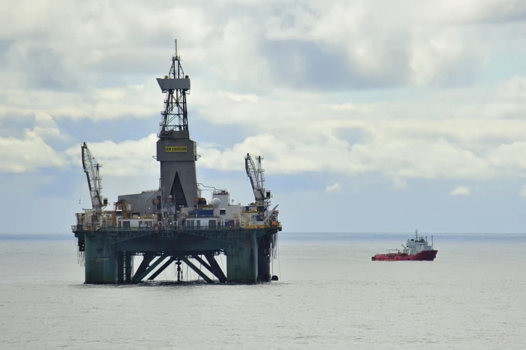 The semi-submersible drilling rig Leiv Eiriksson operating in the ocean with a small red vessel nearby.