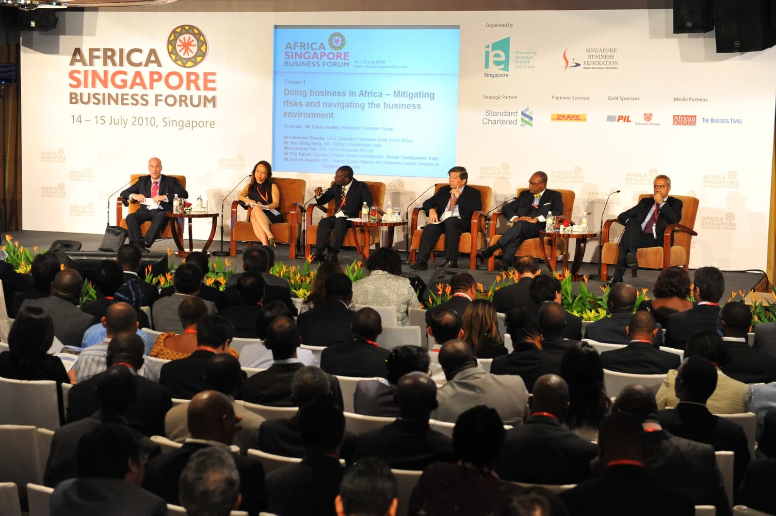 A panel of five individuals seated on a stage, addressing an audience at a business forum.