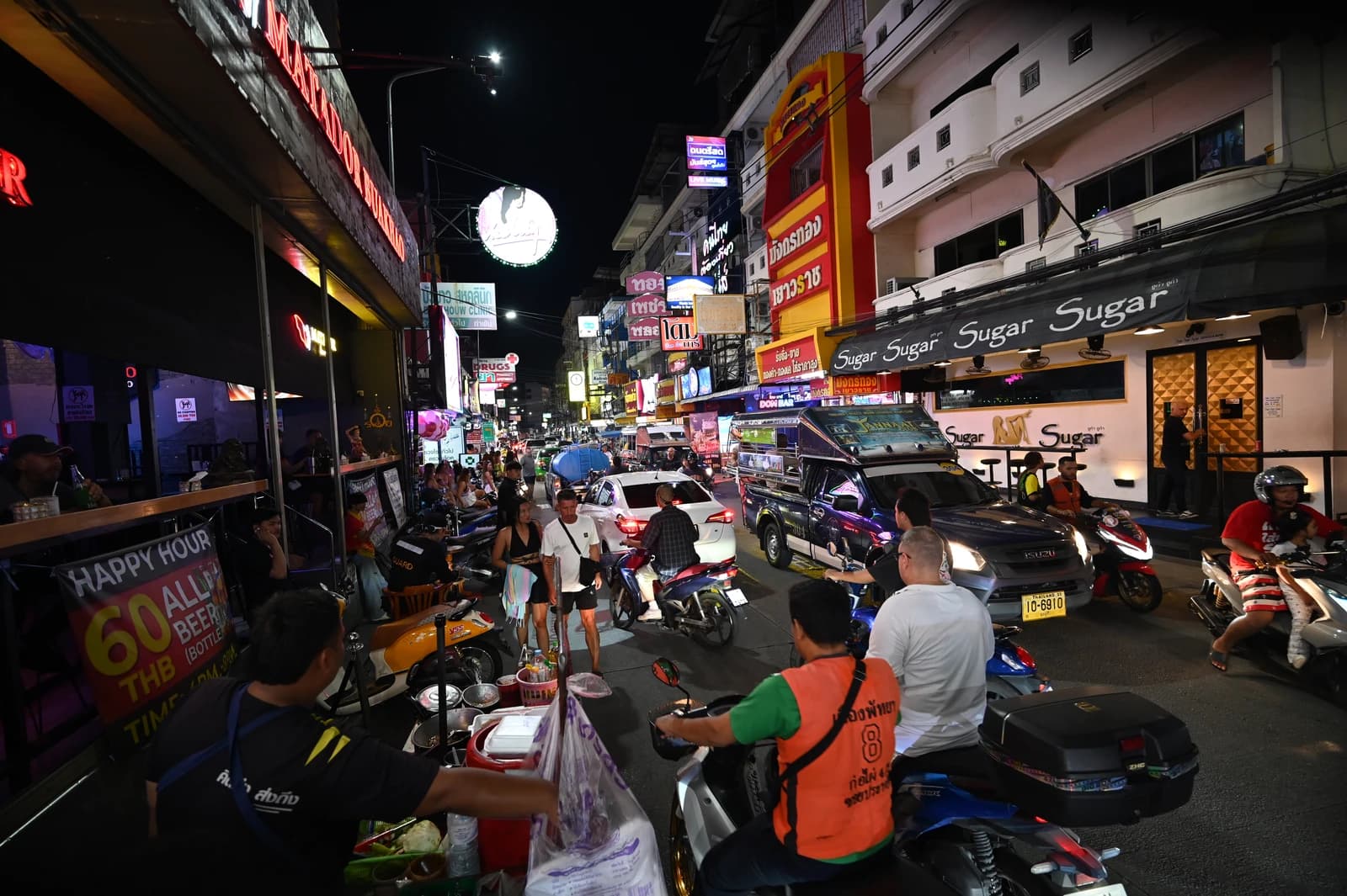 Busy street at night with cars, scooters, pedestrians, and neon-lit buildings.