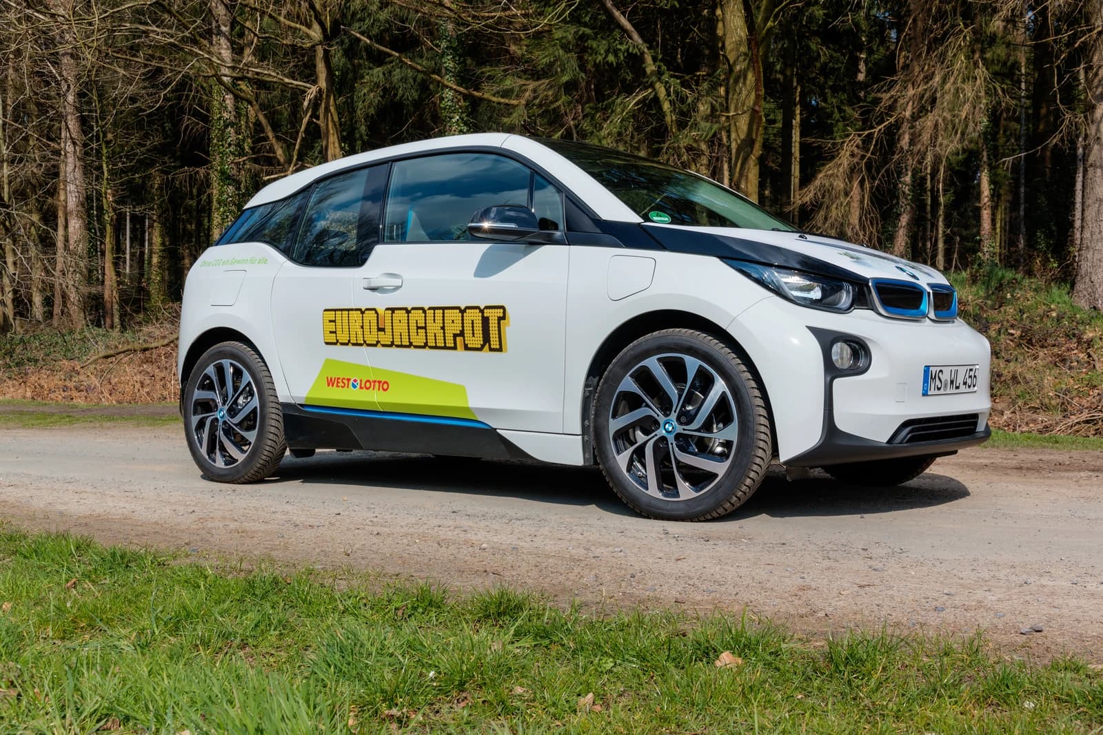 White BMW i3 electric car parked on a dirt road next to trees.