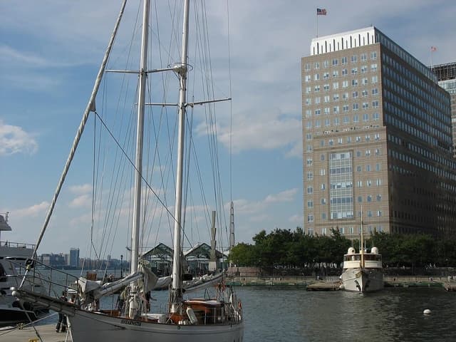 NYMEX building, a large brown office tower, overlooks a harbor with sailboats in Manhattan.