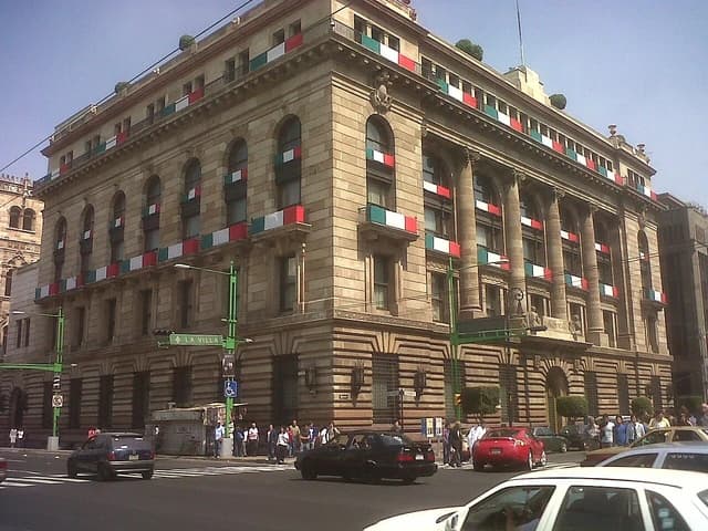 Exterior of the Banco de México Bicentenario building on a clear day with cars and pedestrians.