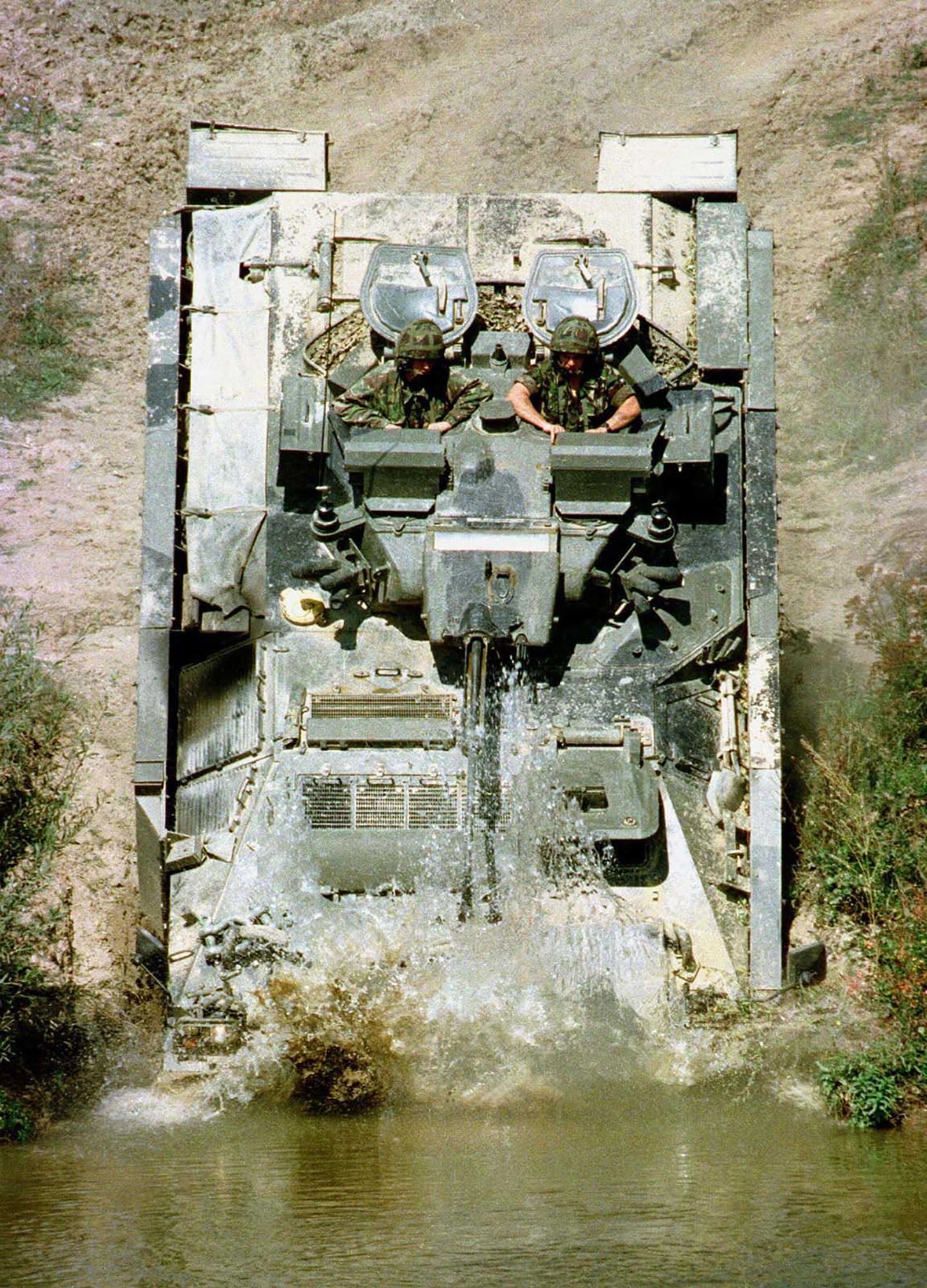 Two soldiers in military vehicle traversing water in Kosovo.