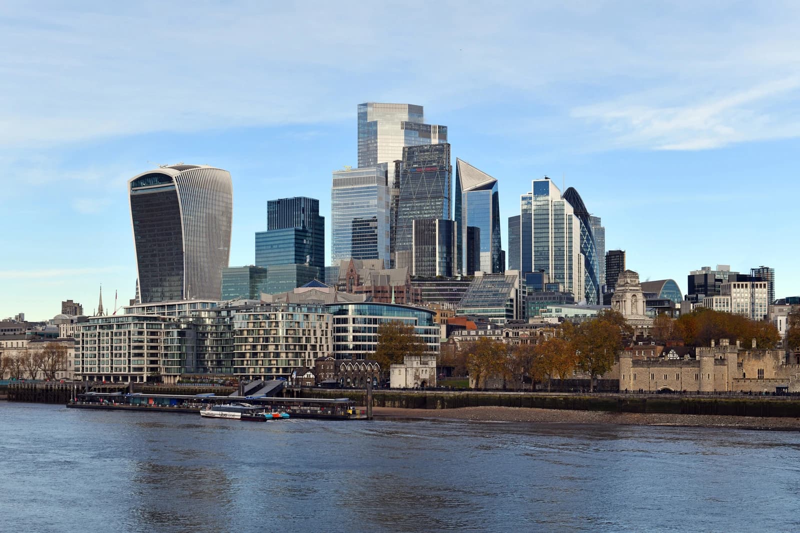 City of London financial district skyline with modern buildings and the River Thames in the foreground.