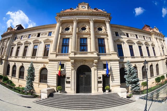 Grand neoclassical building of the National Bank of Romania, with flags and a blue sky.