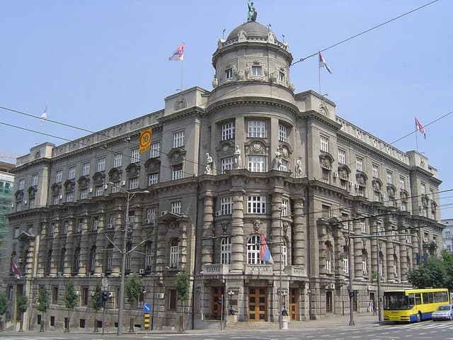 Exterior view of the Serbian Government building, a large stone structure with flags.