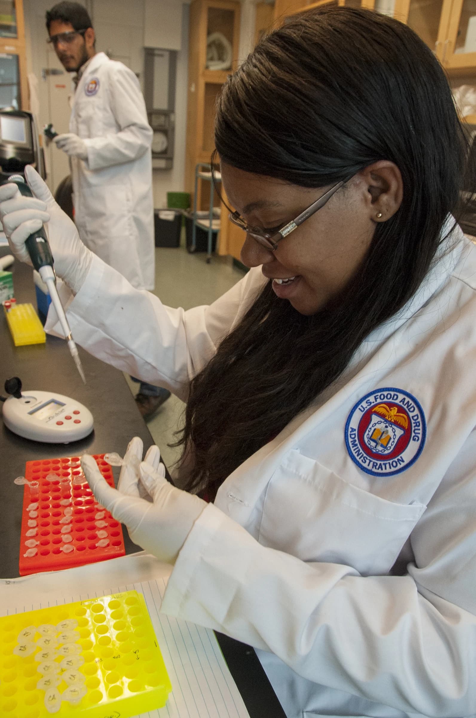 A scientist wearing glasses and a lab coat pipetting samples in a laboratory.