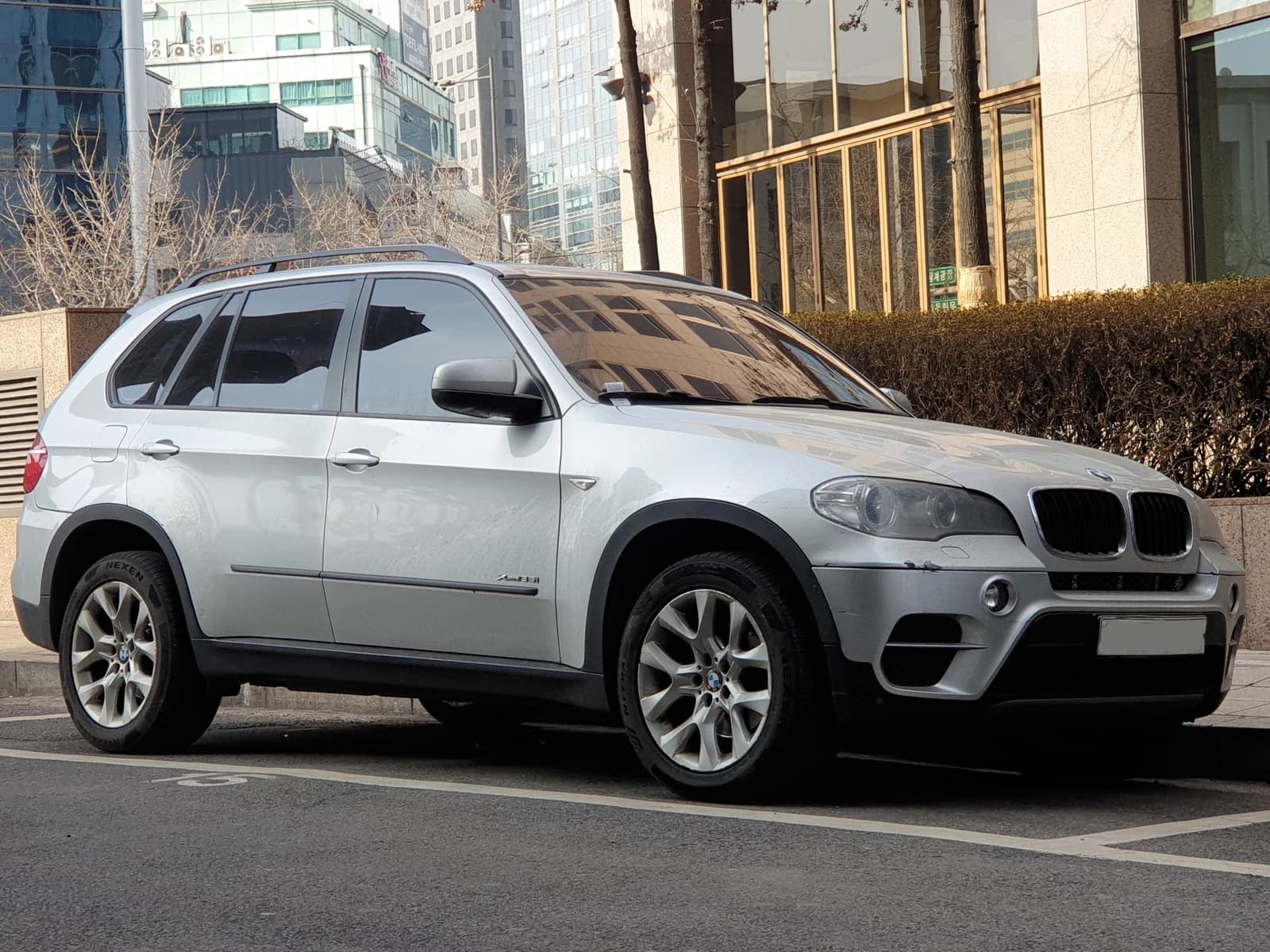 A silver BMW E70 X5 xDrive35i SUV parked on an urban street.