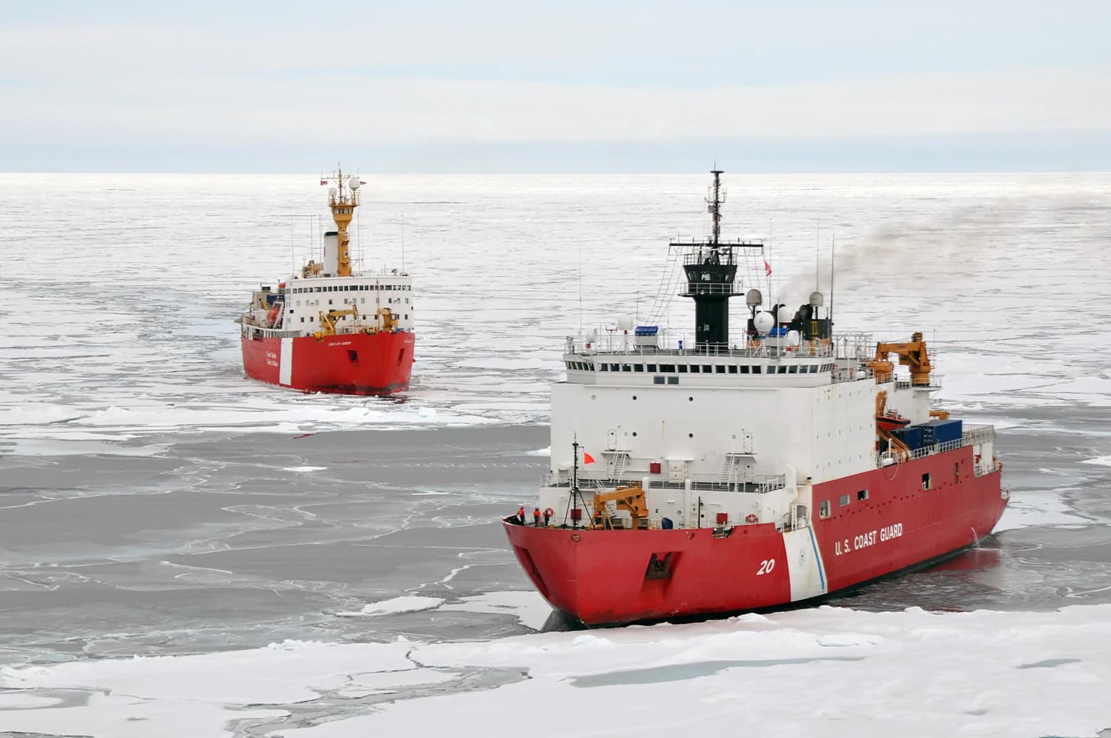 Two red and white icebreaker ships, Louis S. St-Laurent and Healy, moving through an icy Arctic ocean.