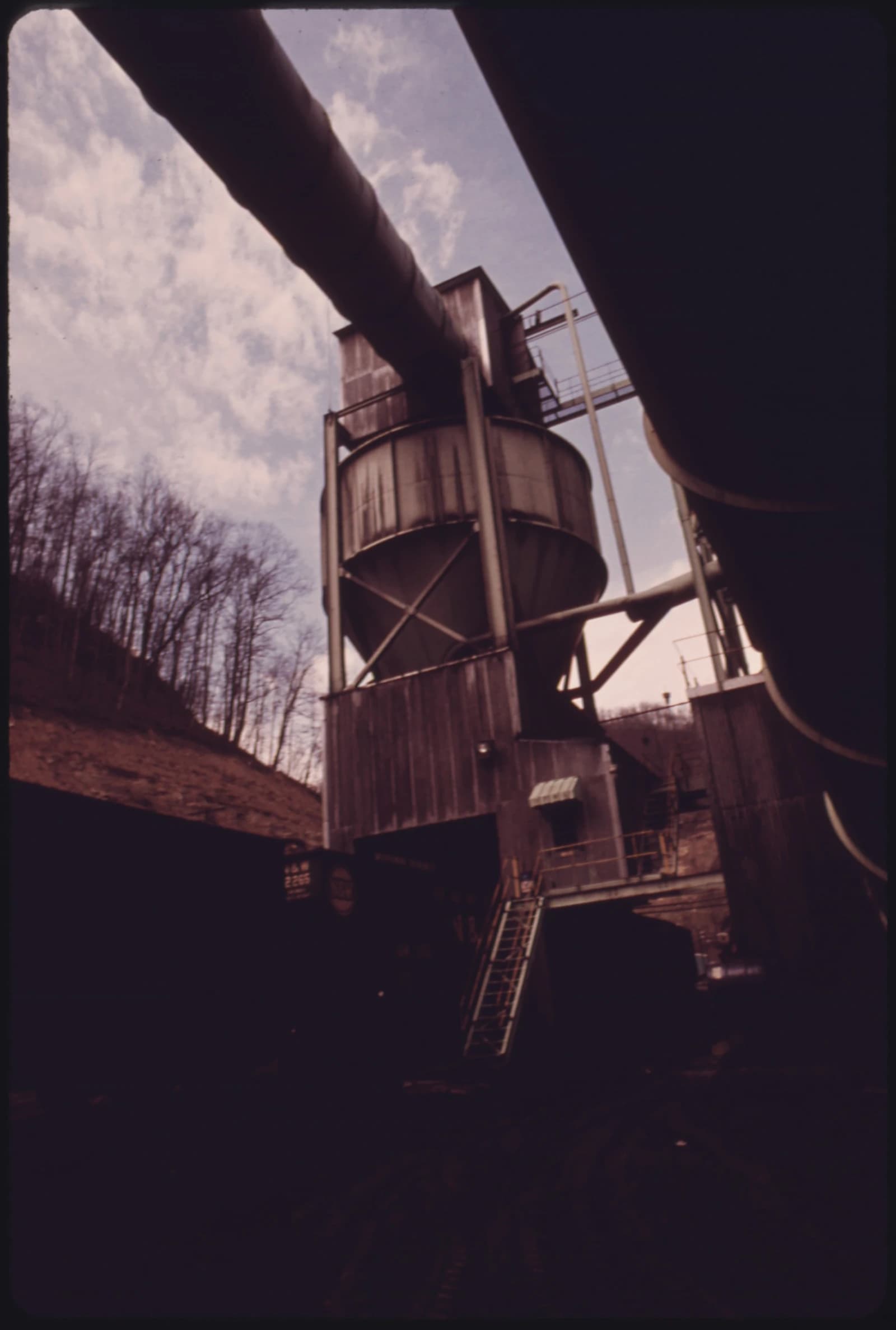 A large coal tipple structure with conveyors, against a sky and bare trees.