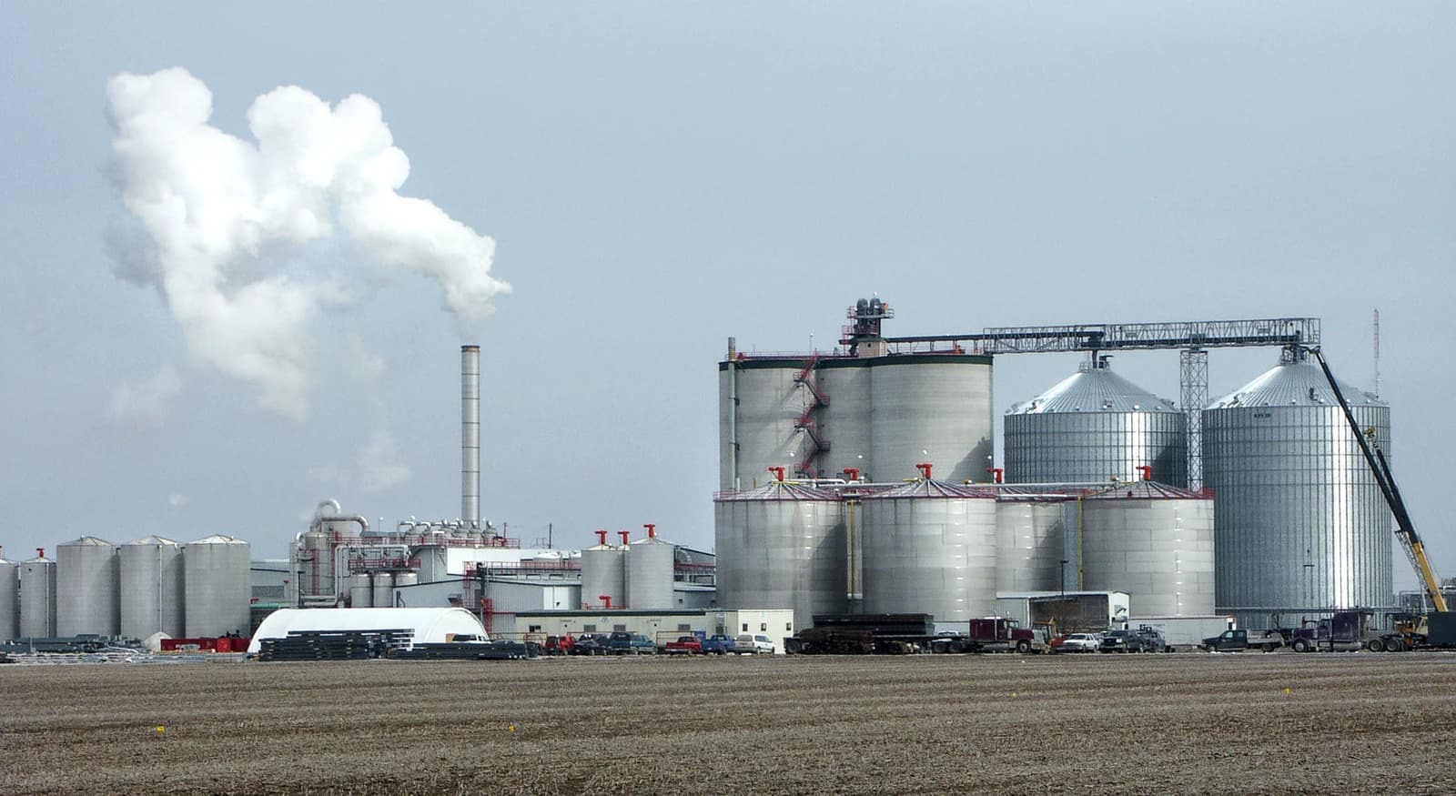 An ethanol plant with multiple large storage tanks and a tall smokestack emitting steam.
