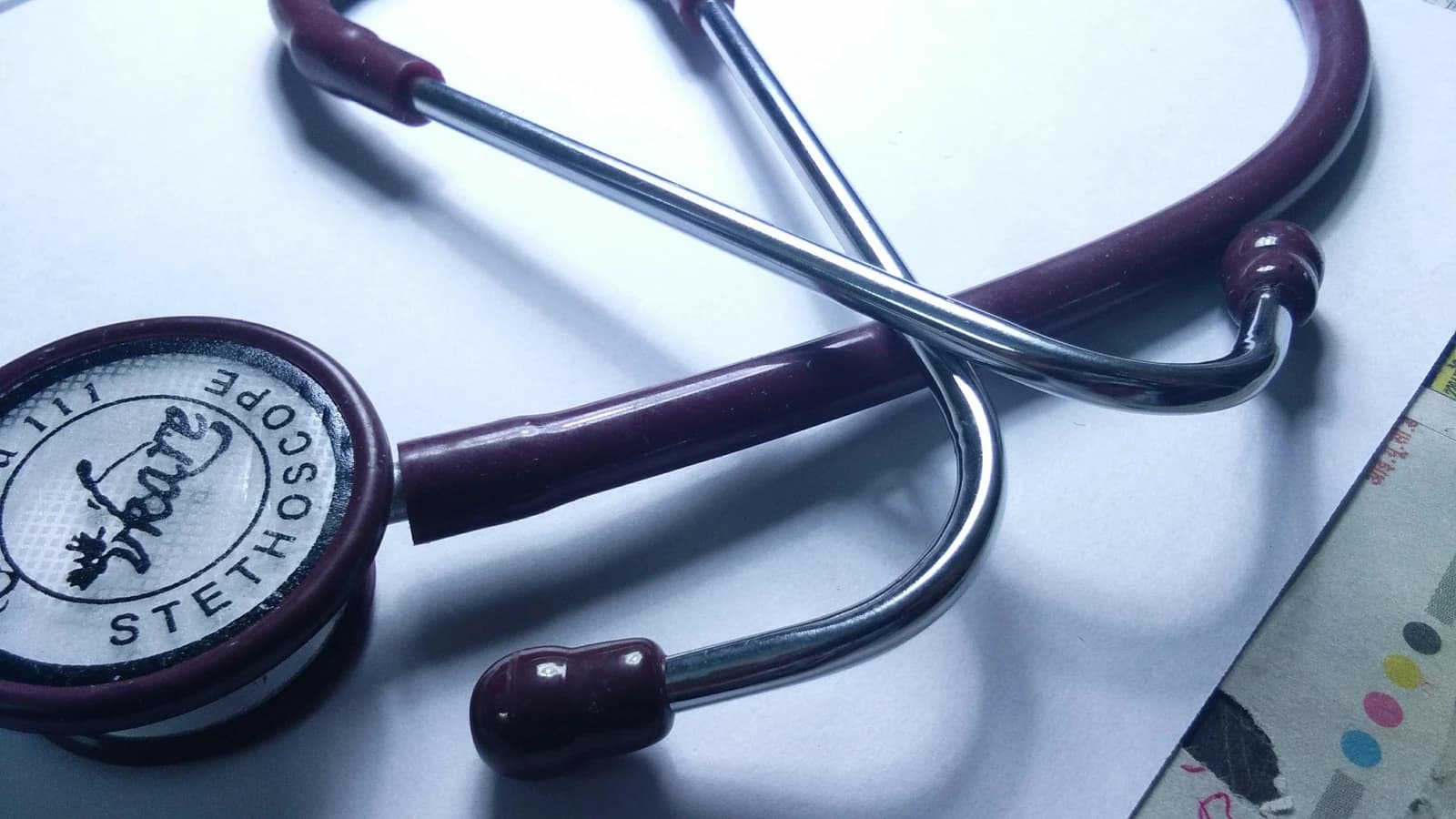 A maroon and silver stethoscope rests on a white surface.