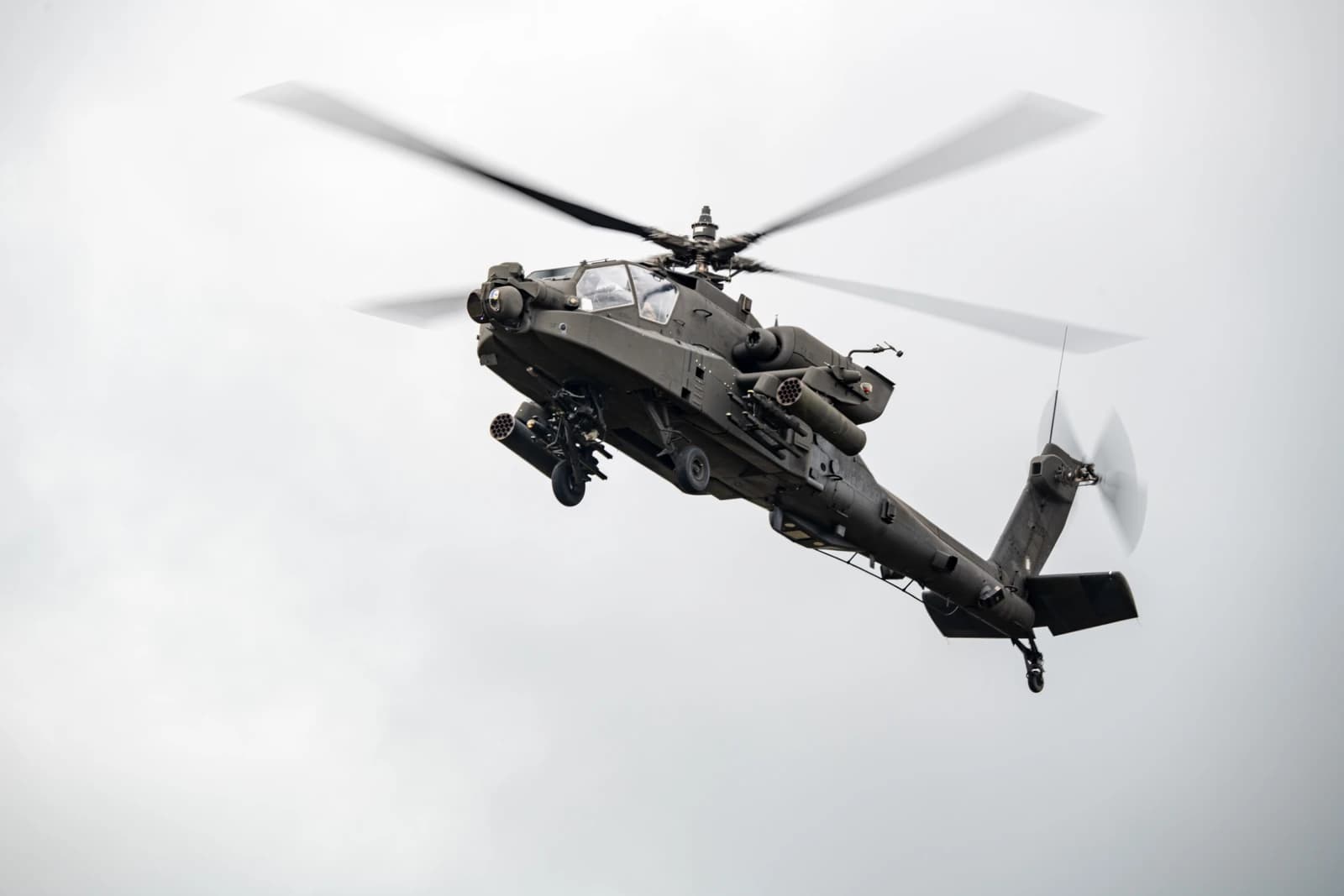 US Apache attack helicopter in flight against a cloudy sky during military exercise.