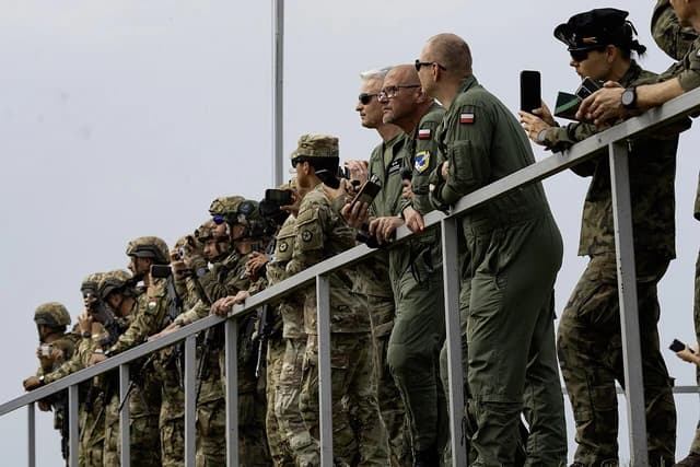 US and Polish military personnel observing an event from a raised platform.