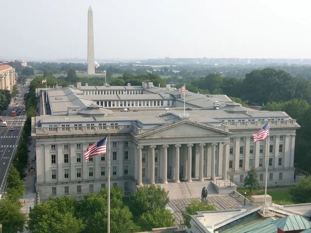 The United States Treasury Building in Washington D.C., with the Washington Monument visible.