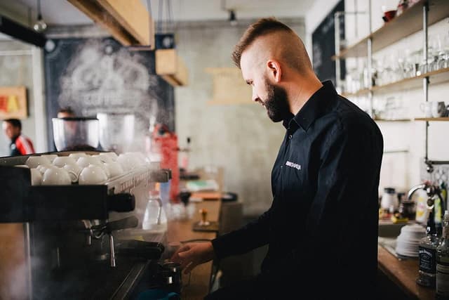 Barista prepares coffee using an espresso machine in a modern cafe.