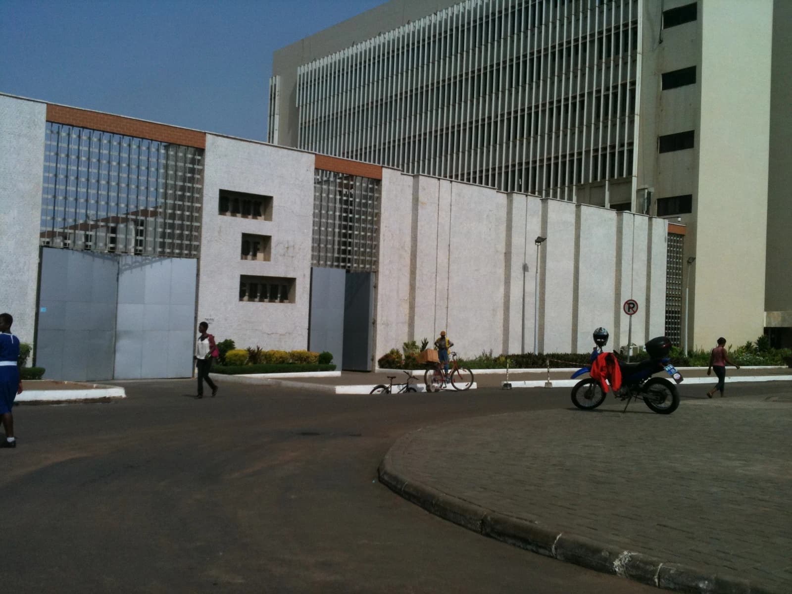 Bank of Ghana building exterior with people walking and a motorcycle parked.