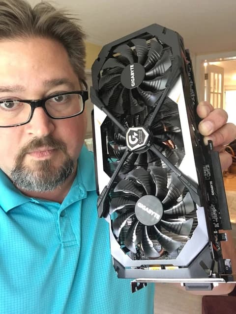 Man with glasses and a beard holding a large graphics card with two fans.