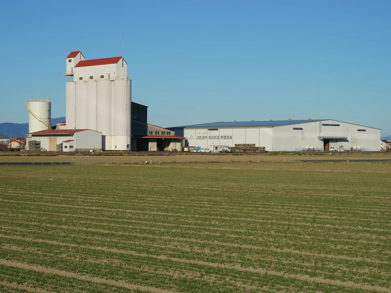 JA Saga South Refrigerated rice storage warehouses next to green agricultural fields.