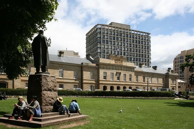 People sitting on the base of a statue outside a large stone government building.