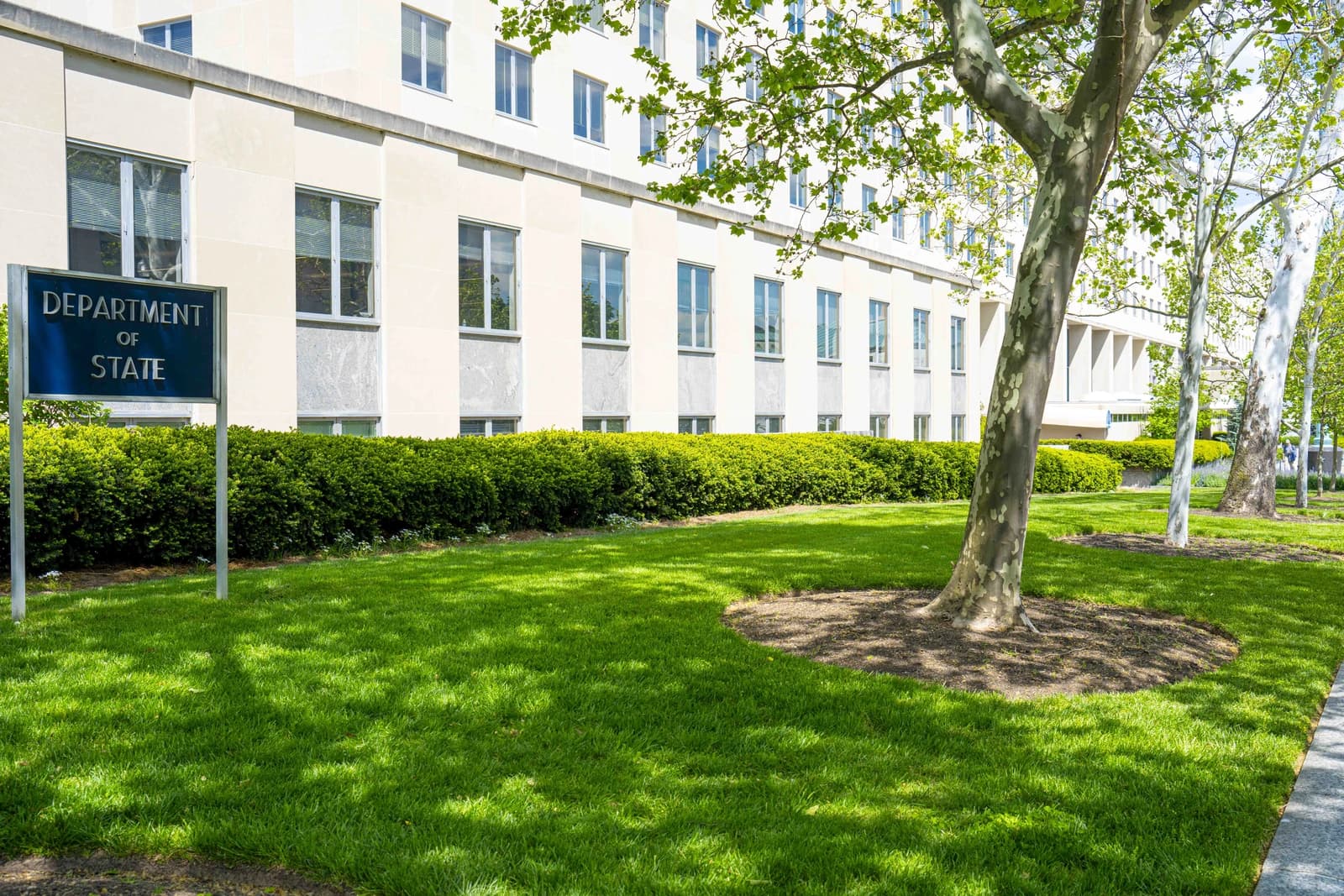 The exterior of the U.S. Department of State building with a sign and green lawn.