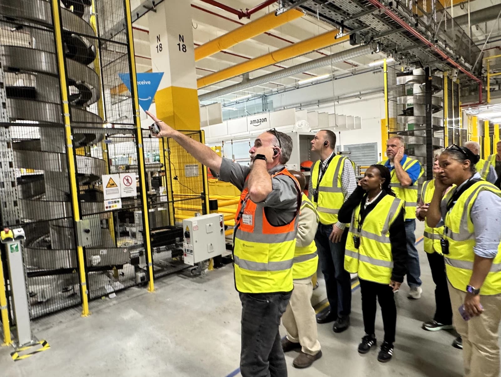 People in high-visibility vests looking at machinery inside an Amazon fulfillment center.
