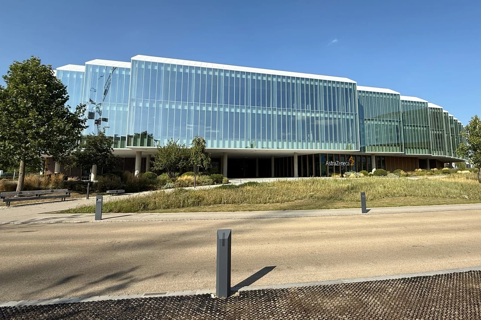 A modern glass building, identified as AstraZeneca, seen from across a road.