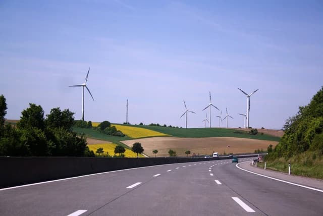 Wind turbines on a green and yellow field next to a highway in Germany.
