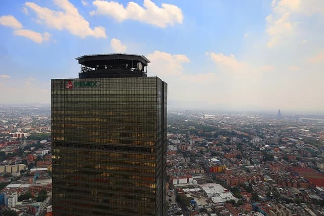 An aerial view shows the Pemex Tower, a large skyscraper, dominating the Mexico City skyline.