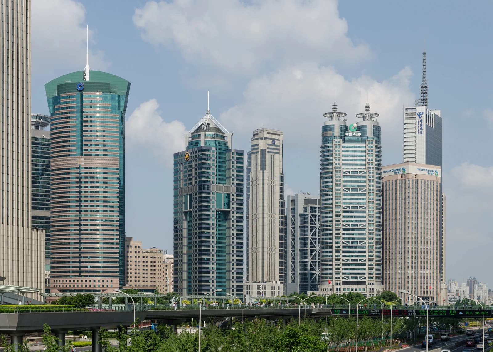 Skyscrapers in Shanghai's Lujiazui financial district with an elevated pedestrian bridge in the foreground.