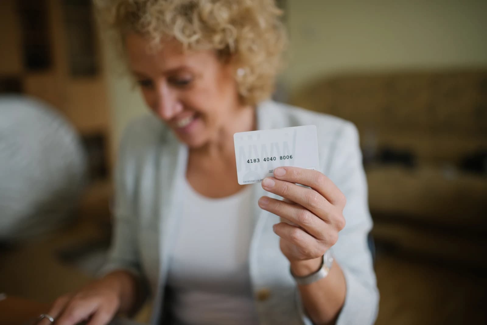 Woman holds a white plastic card with a credit card number.