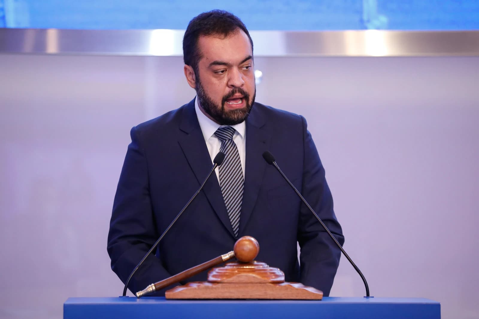 Cláudio Castro, former Rio governor, speaking at a podium with a gavel.