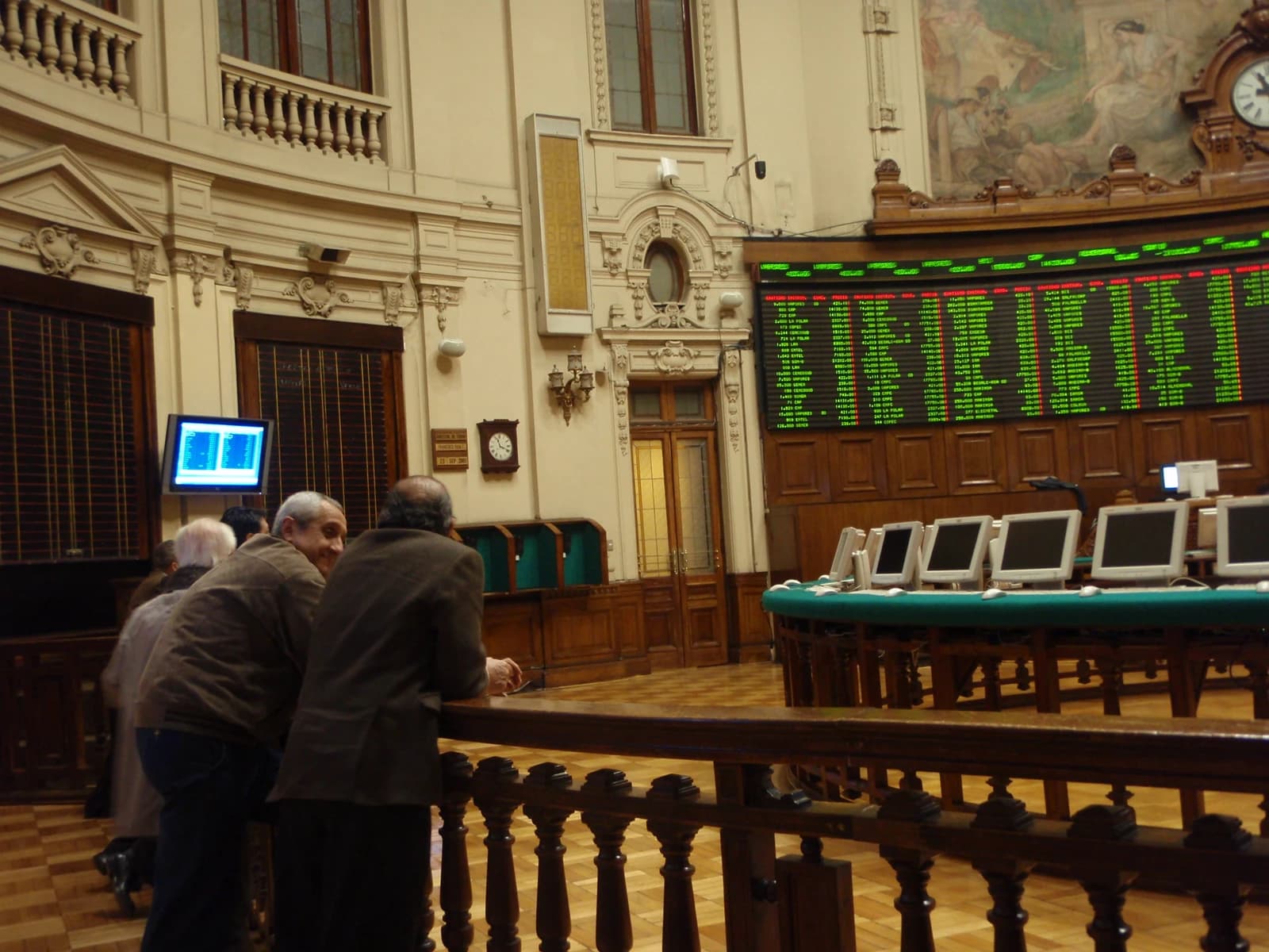 People observe a stock market display board in the main hall of the Bolsa de Comercio.