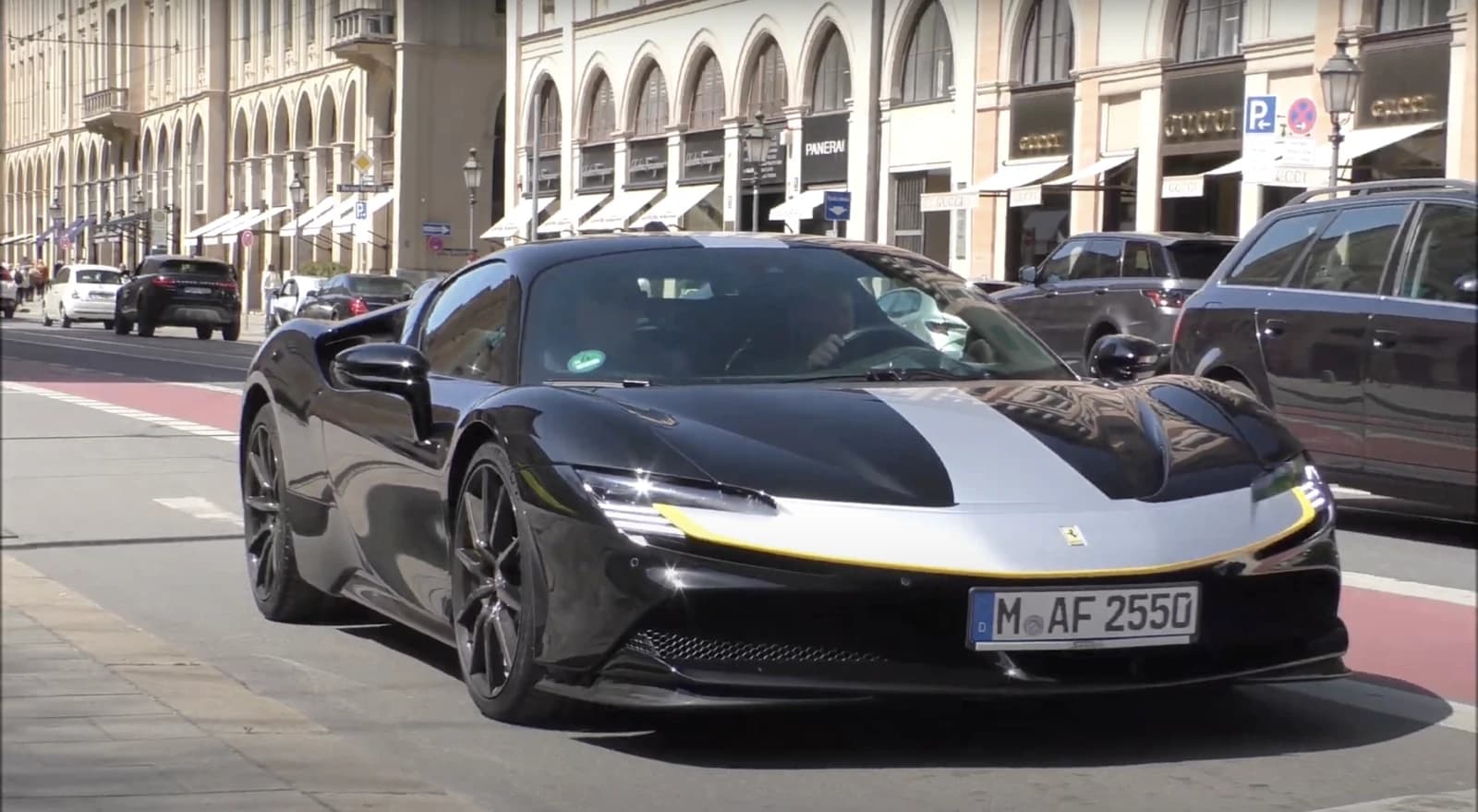 Black Ferrari SF90 Stradale Assetto Fiorano with a silver racing stripe driving on a city street.