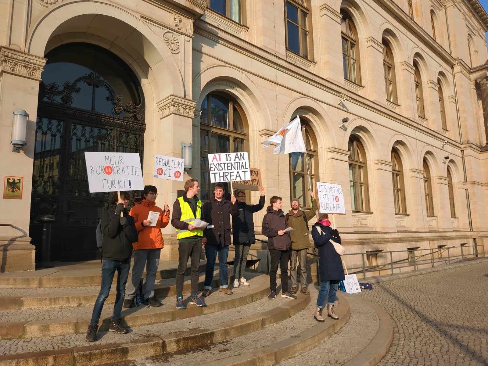 People demonstrating with signs about artificial intelligence regulation on steps of a building.