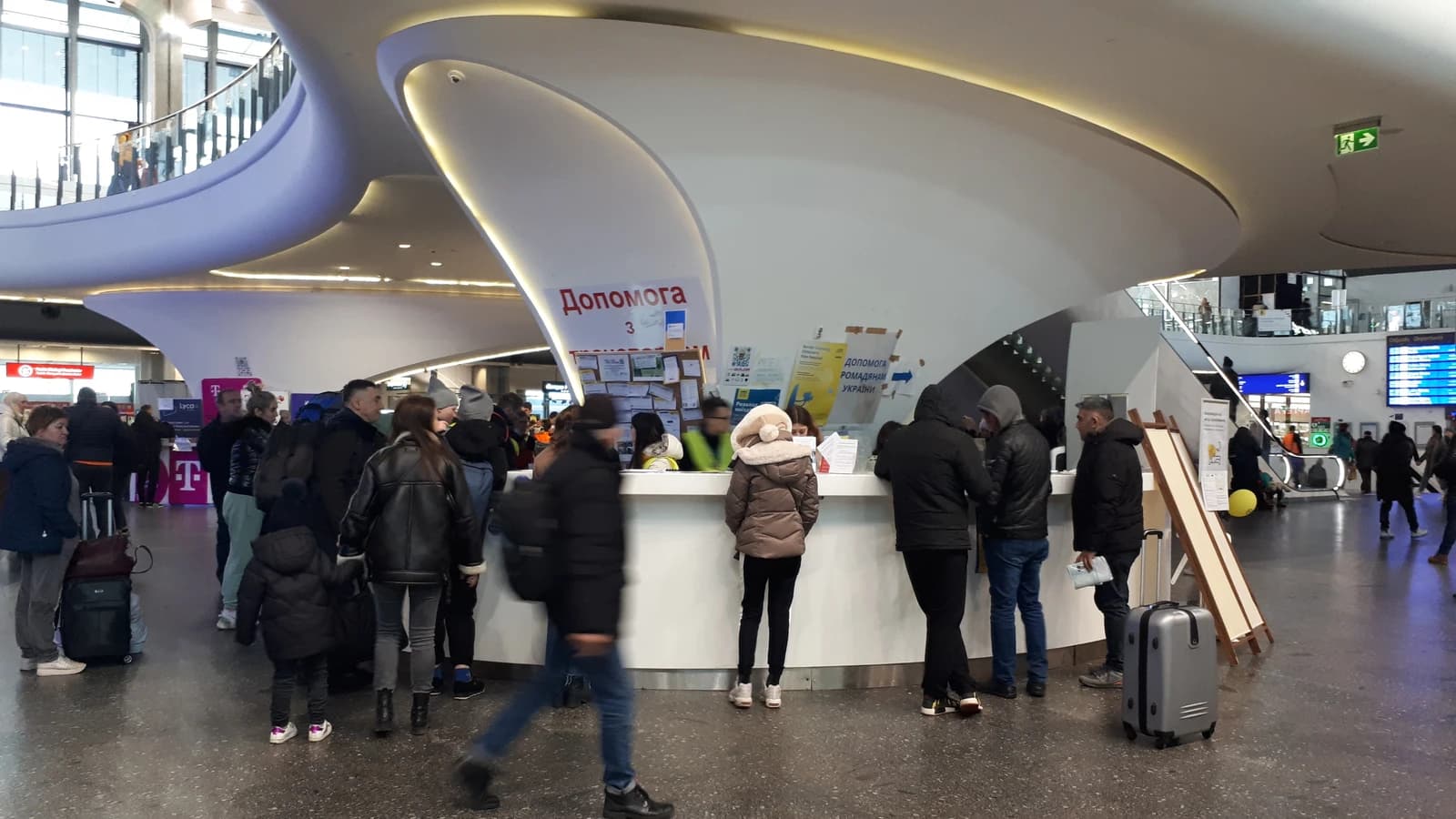People stand at a help desk for Ukrainian citizens in a modern building in Warsaw.