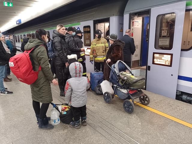 People with luggage and a stroller waiting on a train platform in Warsaw.