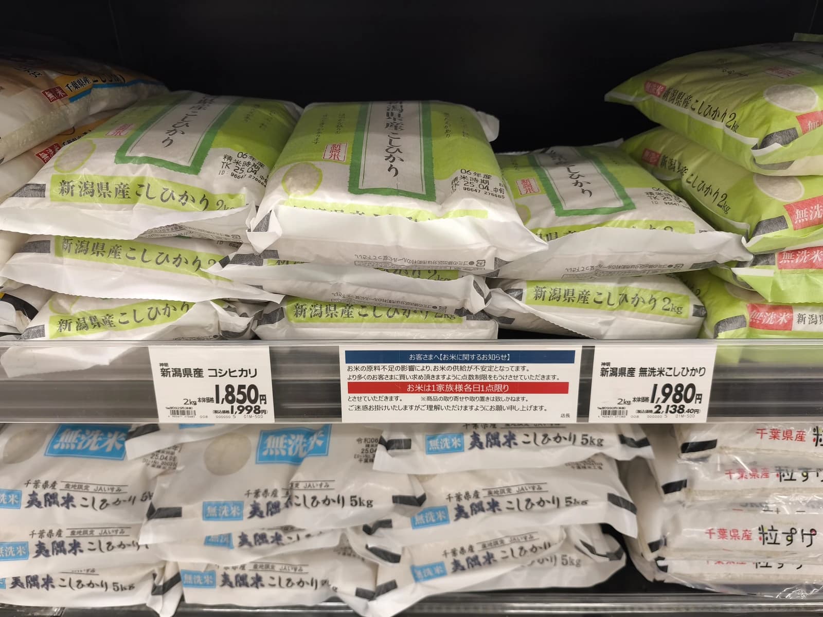 Bags of rice on shelves in a Japanese supermarket, some with visible price tags.