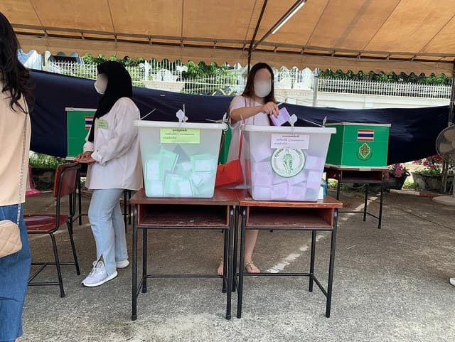 People placing ballots into clear voting boxes at a Bangkok polling station.